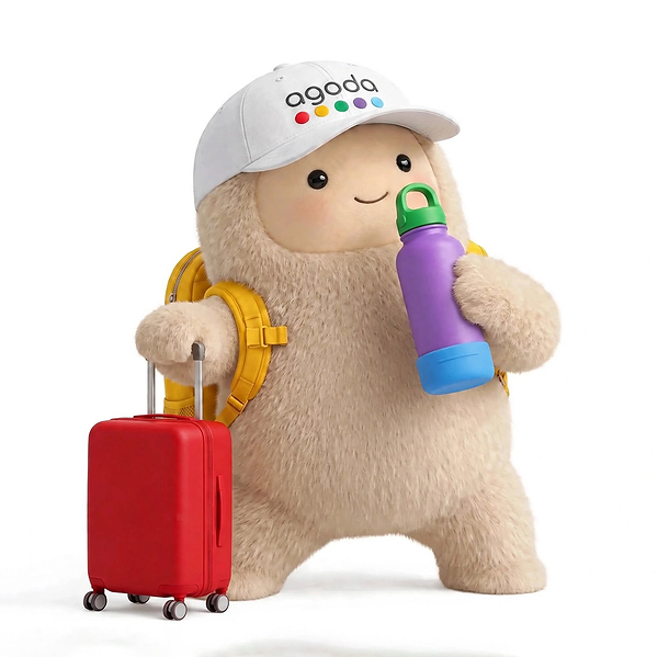 Meta’s Muse character Jolly wearing an Agoda-branded cap beside a suitcase